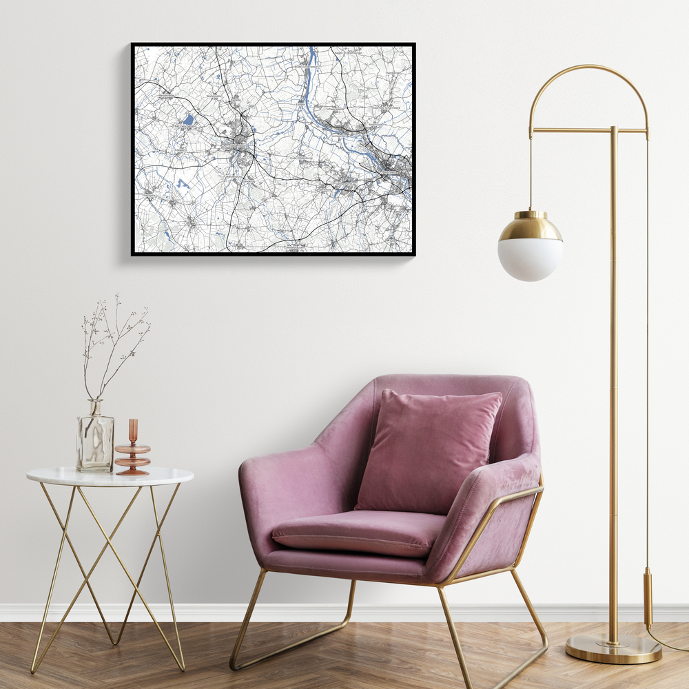 Carte géographique personnalisée encadrée en noir au-dessus d’un fauteuil rose, près d’un lampadaire doré