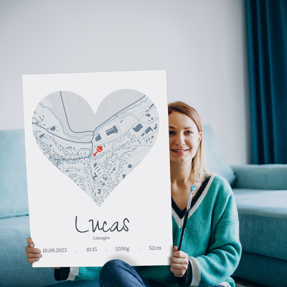 Affiche de naissance sans cadre avec plan de ville en cœur gris et prénom, devant un canapé bleu